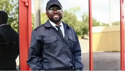 Homem vestido de segurança sorrindo em frente a uma porta